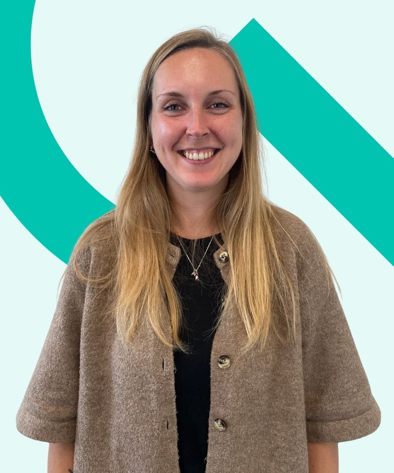 Sarah i hvid skjorte med TEKNIQ Kvalitet-logo, smilende foran et lyst kontormiljø.